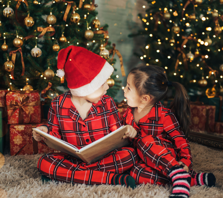 Young boy with Santa hat and young girl looking in awe at each other while reading a book