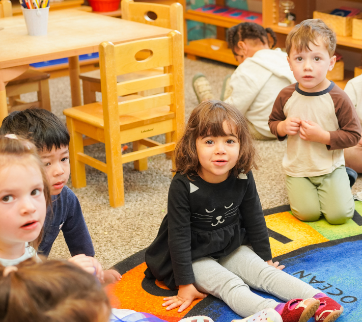 Young children sitting on the floor round a rug with a globe on it.
