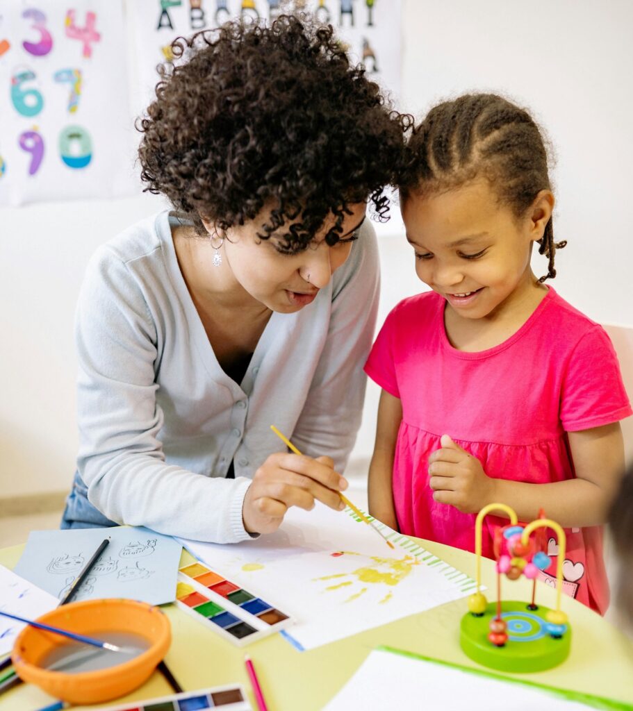 Woman helping preschool girl with project