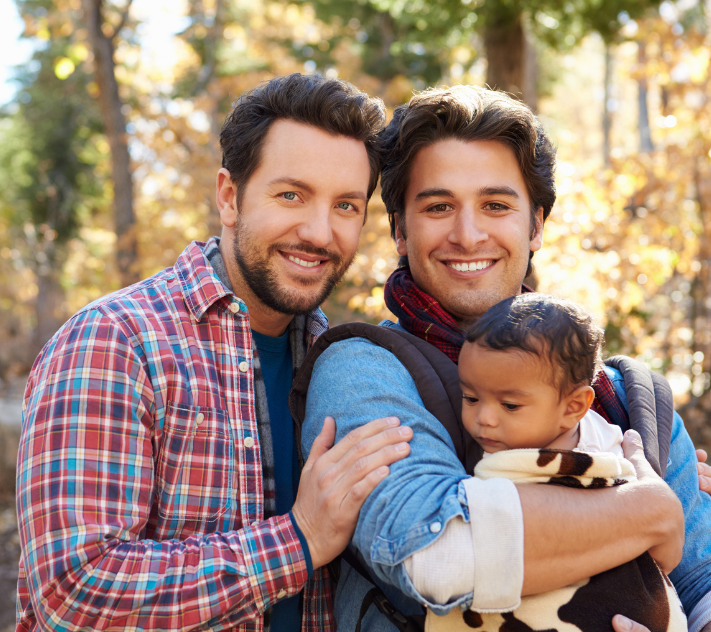 Two fathers smiling while one is holding their son.