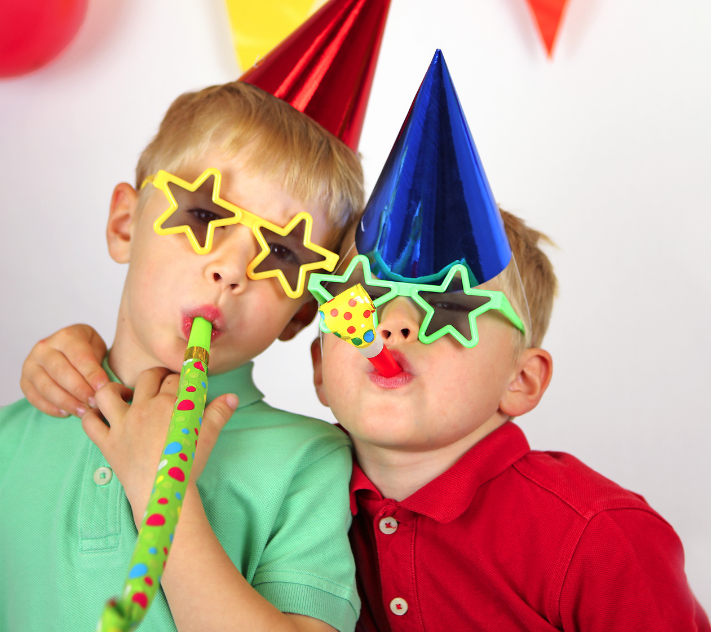 Two young boys with birthday hats and star sunglasses on blowing sound makers.