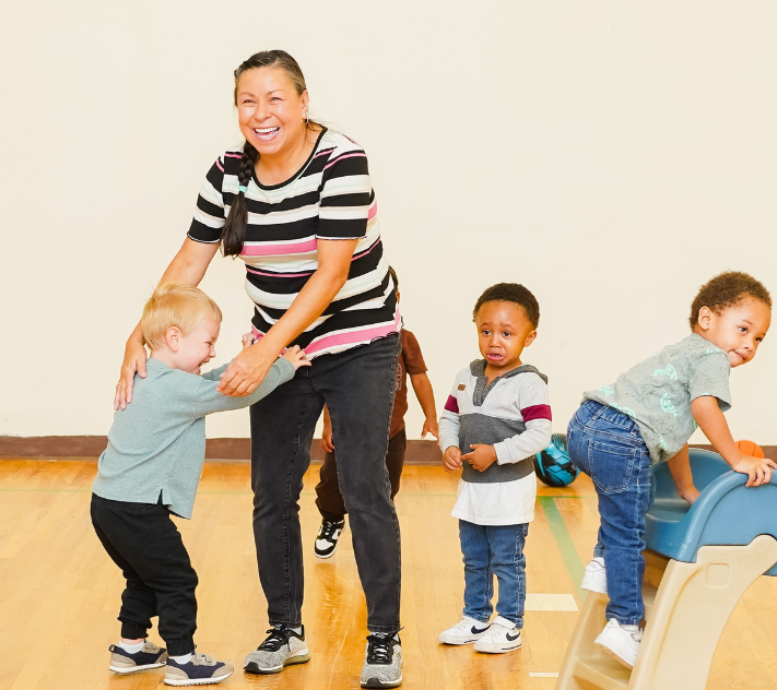 Preschool teacher with three young boys around her playing.