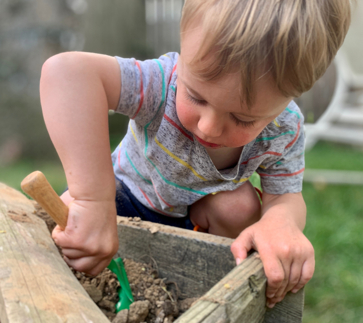 Young boy digging in a dirt garden box with a small shovel