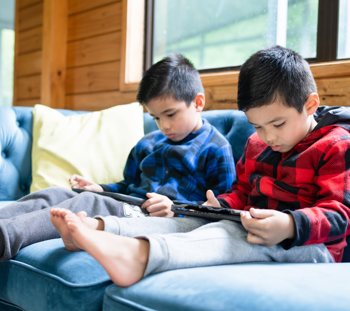 Young boys witting on a cough holding tablets and watching attentively.