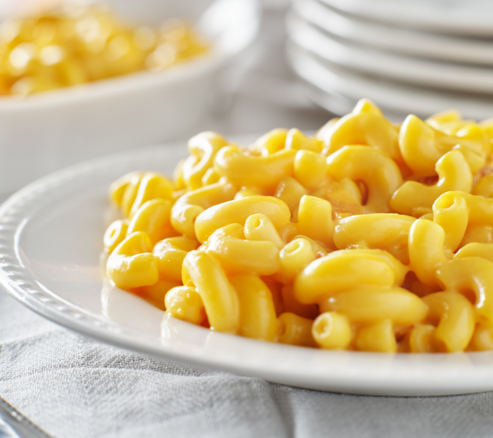 Macaroni and cheese on a white plate with white plates and a bowl of mac n' cheese in the background.